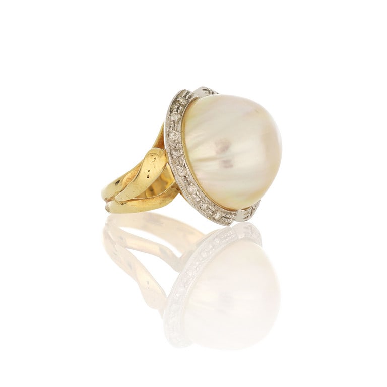Anello in oro giallo con grande perla "Mabè" al: Anello in oro giallo con grande perla "Mabè" al centro e contorno di piccoli diamanti taglio brillante, il tutto sostenuto da un gambo stilizzato a foglia. Misura n. 18. Peso 12,20 g.
