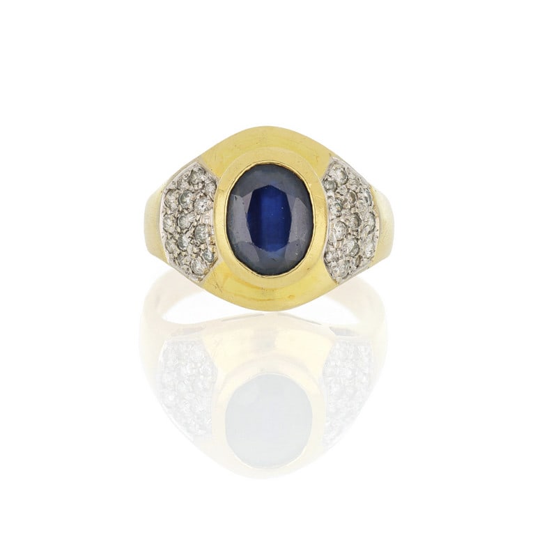 Anello in oro giallo e bianco a fascia, al centro: Anello in oro giallo e bianco a fascia, al centro uno zaffiro australiano di taglio ovale, affiancato da due pavè di piccoli diamanti per complessivi ct. 0,35 ca. Misura n. 19. Peso 8,65 g.