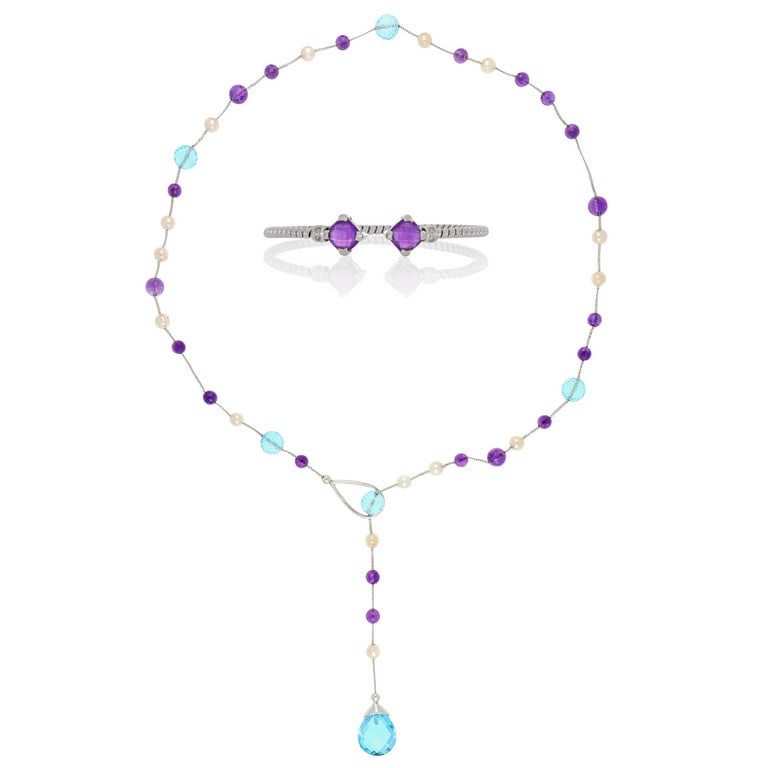 Parure composta da collanina in oro intervallata: Parure composta da collanina in oro intervallata da sfere di topazi azzurri, perle coltivate, quarzi ametista, chiusura passante, e bracciale rigido con ametiste briolettate di forma quadrata. Peso 43