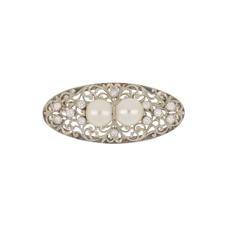 Spilla di forma ovale, realizzata in oro bianco: Spilla di forma ovale, realizzata in oro bianco traforato e inciso a volute floreali, al centro due perle di coltura 9,5 mm di diametro e piccoli diamanti taglio brillante per ct. 1,0 ca. Dimensioni 5