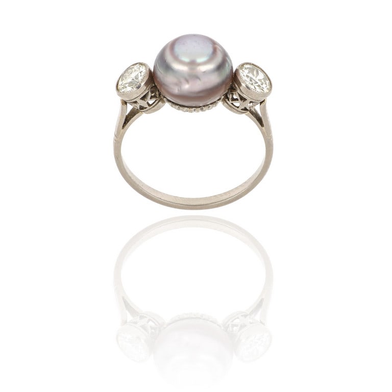 Anello in oro bianco di antica manifattura, al: Anello in oro bianco di antica manifattura, al centro una perla naturale di acqua salata grigia, 9,90 mm di diametro, ai lati due diamanti di taglio antico per ct. 0,70 ca. Misura n. 13. Peso 3,94 g.