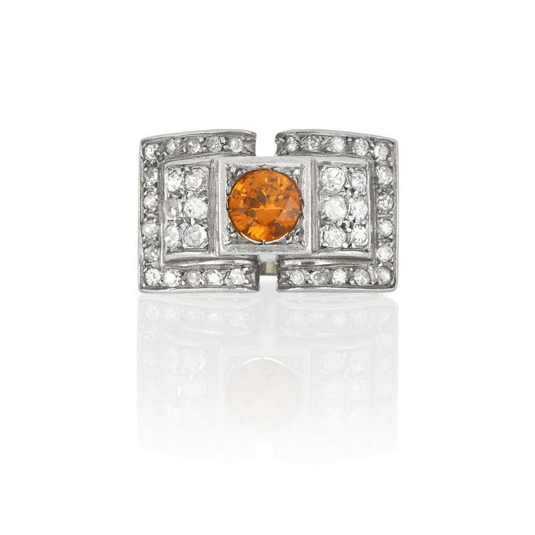 Anello in platino tipo Tank con pietra arancione: Anello in platino tipo Tank con pietra arancione centrale, sulle volute diamanti di forma rotonda taglio 8/8. Misura 18. Peso 15,06 g.