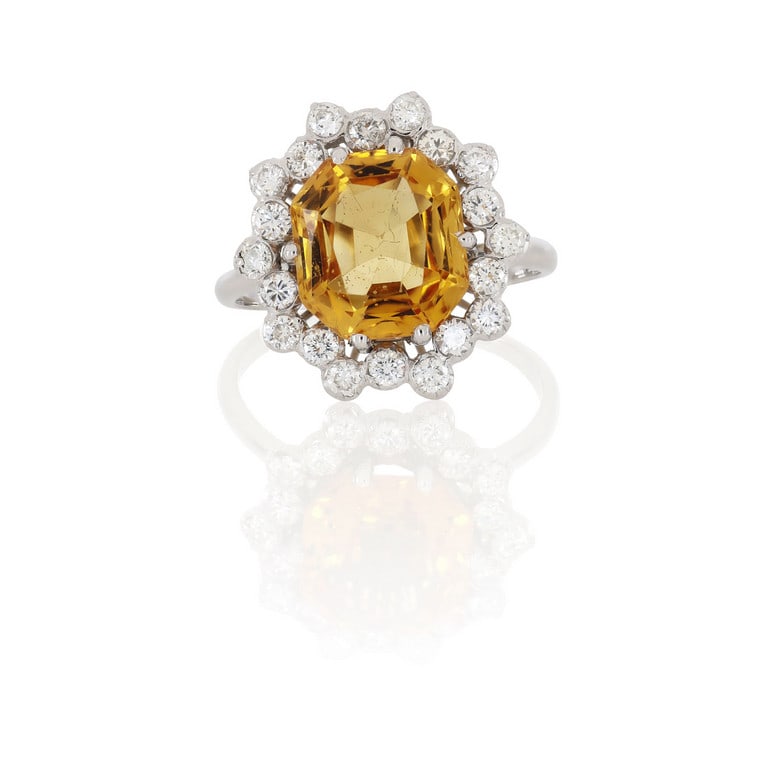 Anello in oro bianco con topazio dal caldo colore: Anello in oro bianco con topazio dal caldo colore mielato, taglio antico a cuscino, ct. 6,50 ca., contornato da diamanti taglio brillante con questo singolare motivo alternato, ct. 0,70 ca. I topazi n