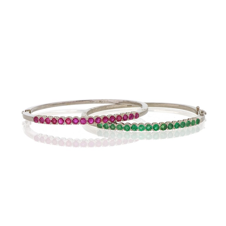 Coppia di bangle rigidi in oro bianco con riviere: Coppia di bangle rigidi in oro bianco con riviere di rubini e smeraldi per un totale di circa 5 ct complessivi. Diametro 60 x 55 mm. Peso 34,21 g.