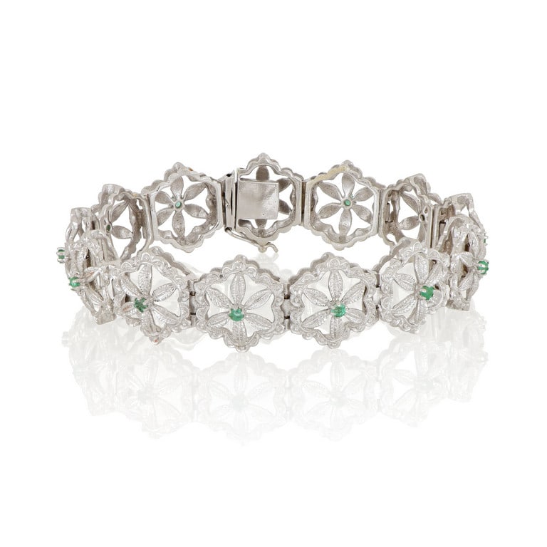 Bracciale in oro bianco con lavorazione a: Bracciale in oro bianco con lavorazione a settori, traforati e incisi a formare fiorellini che si rincorrono, al centro piccoli smeraldini rotondi. Dimensioni 20 x 1,7 cm. Peso 30,31 g.