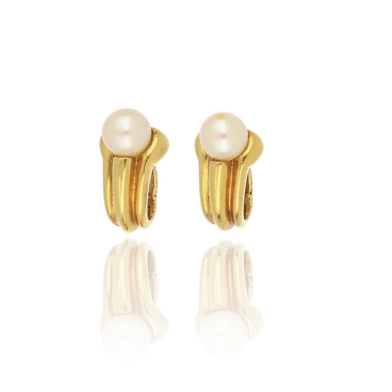 CARTIER - Orecchini in oro giallo a clips,: CARTIER - Orecchini in oro giallo a clips, realizzati con una perla di 7,5/8 mm, sostenuta da un motivo a cornucopia. Firma, punzoni e numeri della manifattura sulla chiusura a clips. Dimensioni 1,5 c