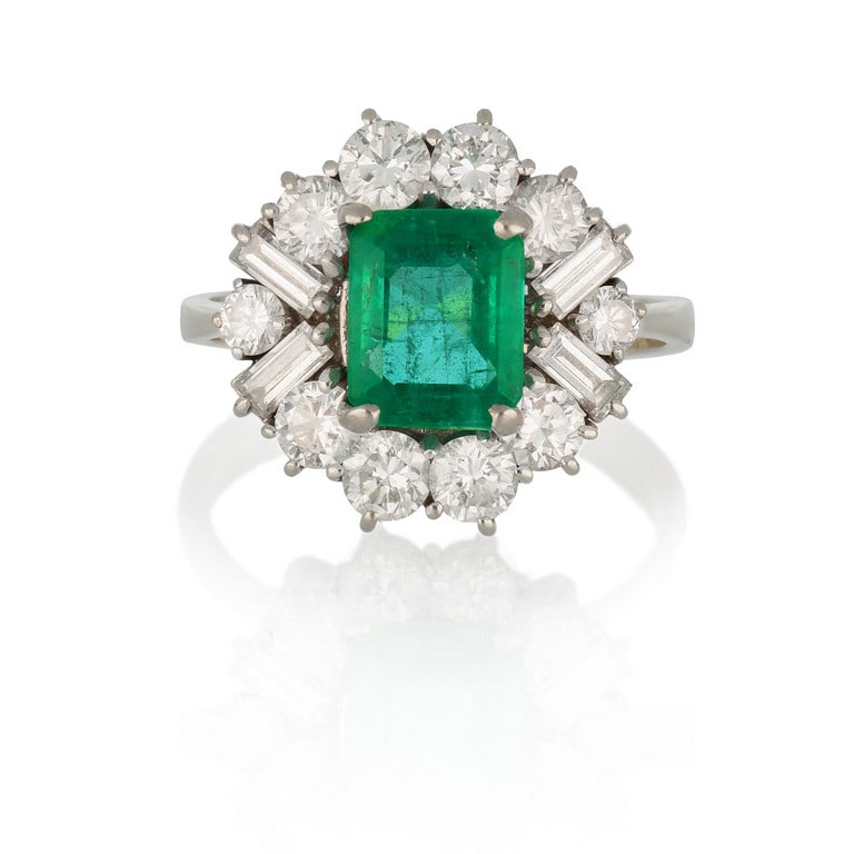 Anello in oro bianco con cluster di diamanti: Anello in oro bianco con cluster di diamanti tondi e baguette per stimati 1,10 ct, al centro smeraldo naturale colombiano di stimati 1,80 ct circa Misura 17. Peso 6,08 g.