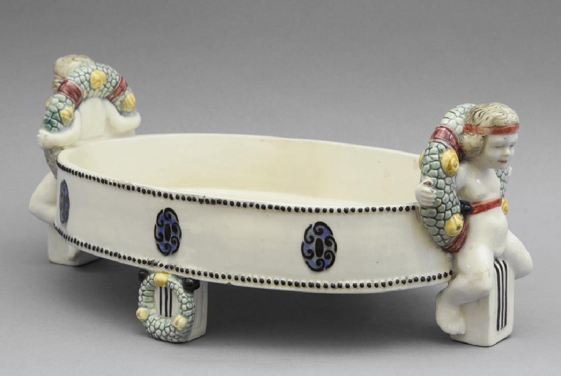 Centrotavola in ceramica bianca decorata in: Centrotavola in ceramica bianca decorata in policromia con putti, s.to Carl Klimt (1876-1945), Vienna inizi sec.XX cm.21x39xh.17