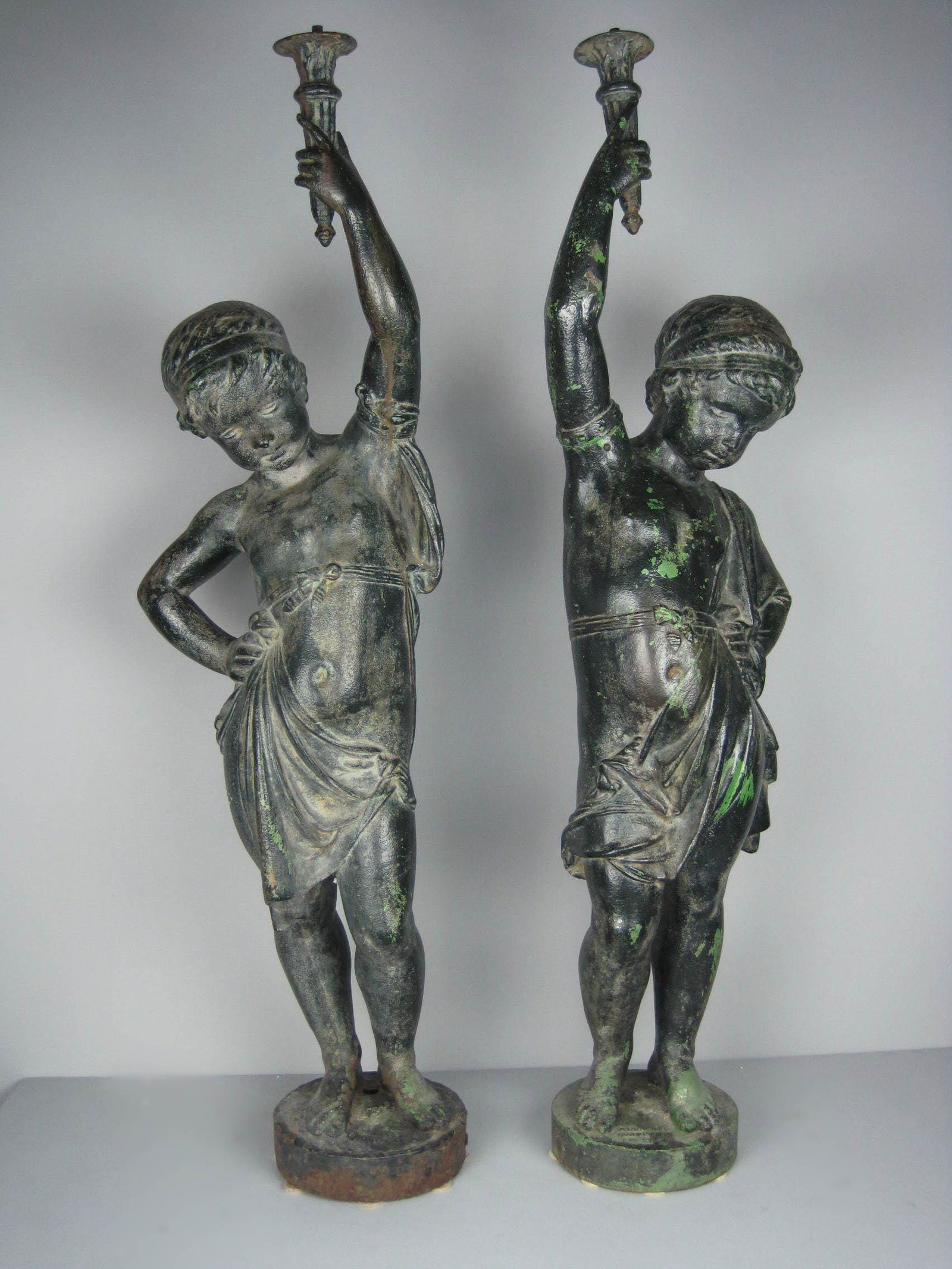 ANTOINE DURENNE Matched French Cast Iron Cupid Statues: Ca. 19th Century A pair of 19th Century cast iron cupid garden statues. Two separate castings marked 'Antoine Durenne' of Sommevoire, France. Both figures take on a sultry and confident stance as they