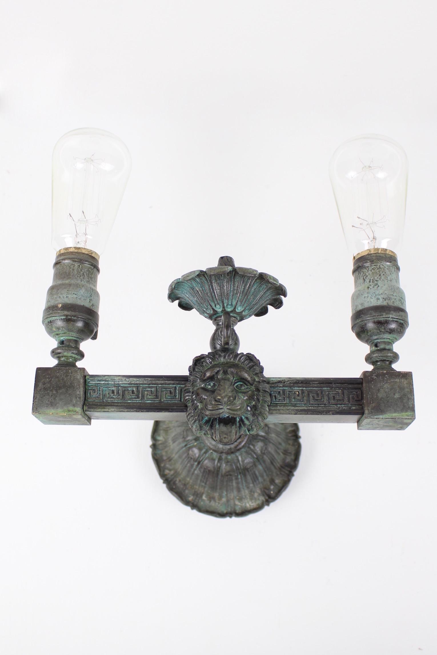 Brass Verdigris Lion Head Sconces (Pair): Circa. 1910 This pair of lion double-arm sconces feature a happy open-mouthed lion â€“ tongue and all! Styled in Greek Revival with a 'greek key' motif. Made out of cast and milled brass. Convert