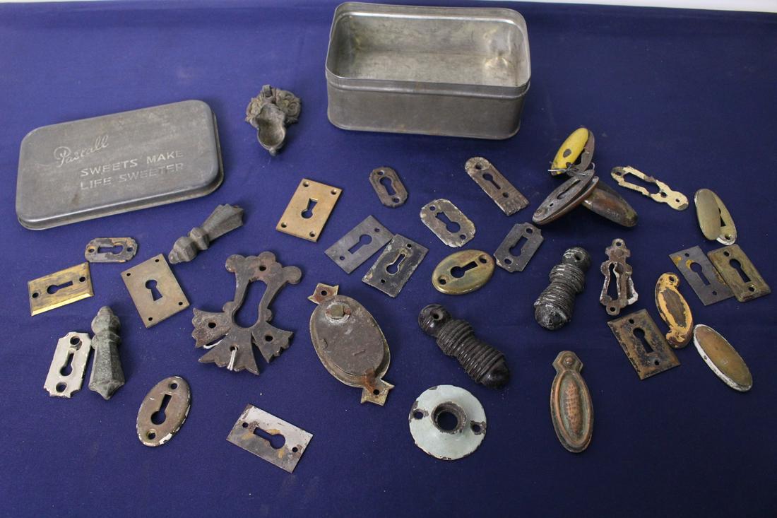 Tin Box of Escutcheons and Keyholes: Tin box of escutcheons and keyholes. 34 pieces. Largest measures 3"x 2.5", smallest measures 1" x 2". Tin box measures 4"x 6"x 2.5"
