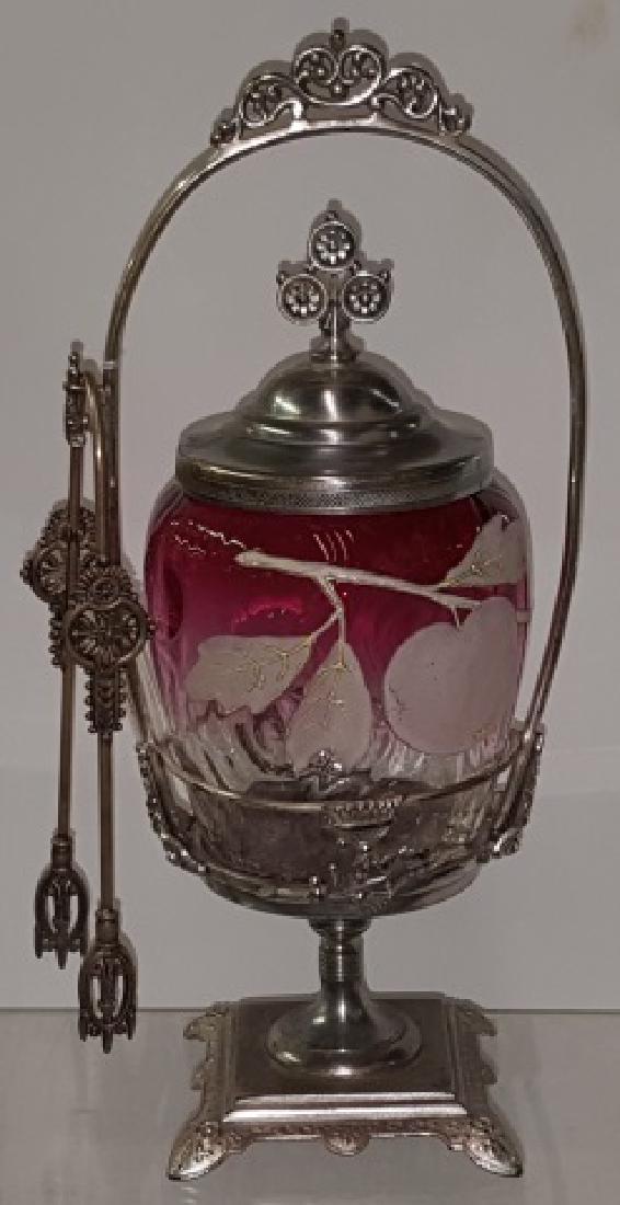 *VICTORIAN PICKLE CASTOR: Having cranberry to clear glass jar with enamel leaf and apple decoration, with silverplate stand, complete with tongs, approximate height 11 1/4".