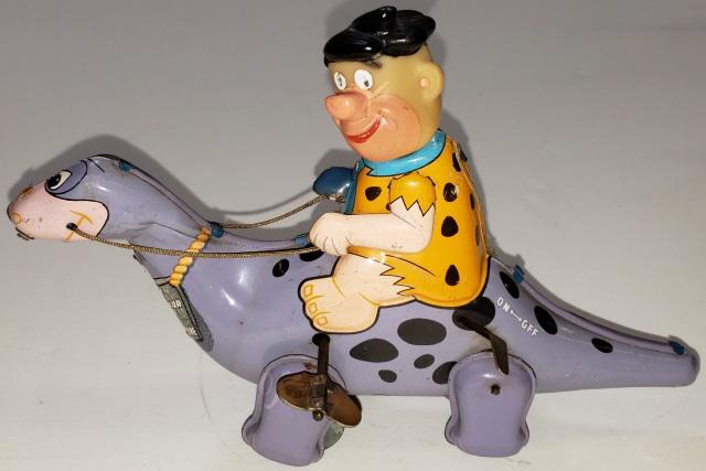 MARX TIN WIND-UP: Fred Flintstone riding Dino, Fred and Dino are tin, Fred's head is rubber, reads "I am Dino - The Dinosaur. If lost, please return me to Fred Flintstone, approximate height 5 3/8", length 8 1/4".