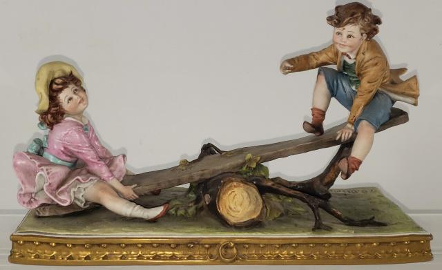 CAPODIMONTE PORCELAIN FIGURE: Boy and girl on seesaw, signed B. Merli, King's Porcelain, height 7 5/8", length 12 3/4".