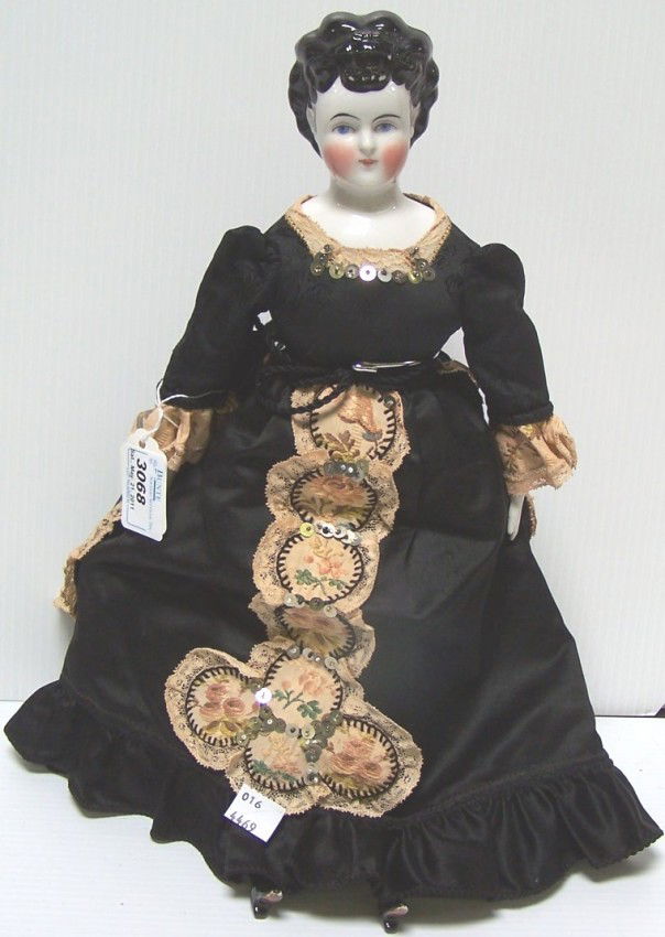 ***CHINA HEAD DOLL: Having black hair, painted features with blue eyes, on cloth body with porcelain arms and legs with painted boots, approximate height 16 1/2''.