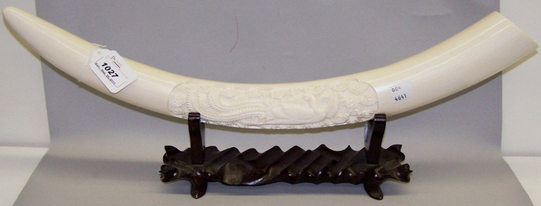 ***CHINESE CARVED IVORY TUSK: Having phoenix bird decoration, approximate length 20 1/2'', raised on hardwood stand. Note: Items containing ivory will only be shipped domestically.