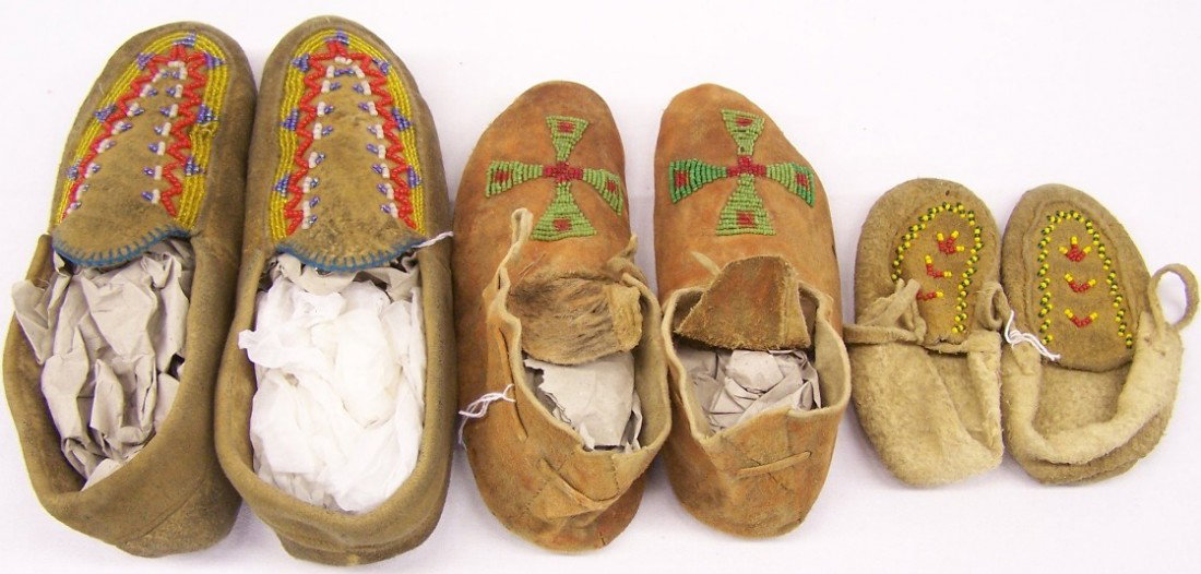 ***THREE PAIR HIDE MOCCASINS: One pair ochre-rubbed and beaded with cross design, the other two pair with soft soles and beaded with multicolor geometric designs, approximate length of longest 9 1/2''.
