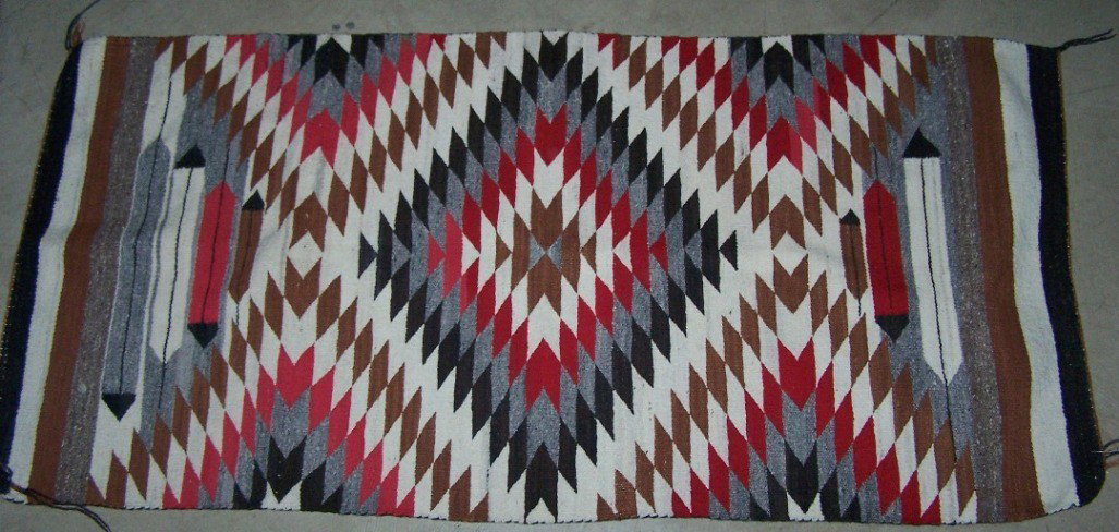 ***NAVAJO WEAVING: Having feather decoration, with geometric design in colors of black, brown, red, gray and white, approximate size 58'' x 28''.