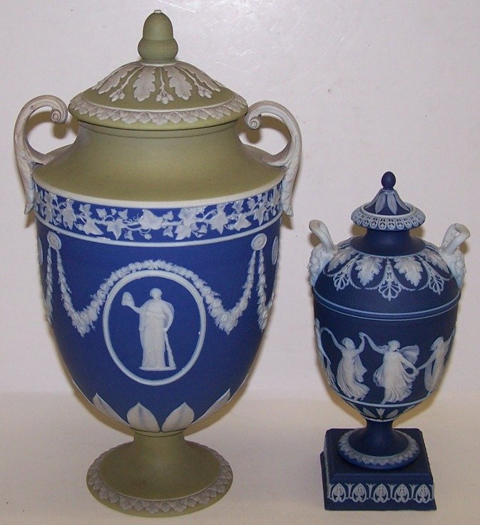 ***TWO WEDGWOOD JASPERWARE TWO-HANDLED COVERED UR: One having classical figural decoration, further enhanced with floral and leaf decoration, impressed on base ''Wedgwood'', approximate height 10 3/4'', one having classical figural decoration against