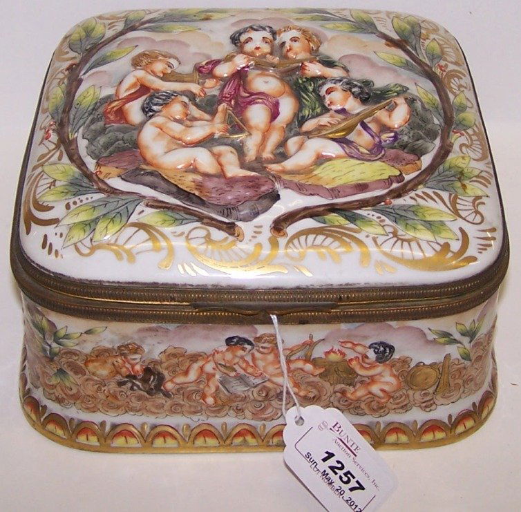 ***19TH C. CAPODIMONTE PORCELAIN BOX: Having relief musical putti decoration, further enhanced with gilt highlight, interior having floral and leaf decoration, base having Capodimonte mark, approximate height 4'', width 7 1/4'', depth 7 1