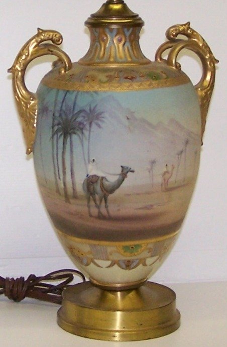 ***NIPPON PORCELAIN TWO-HANDLED VASE: Mounted as table lamp, having desert oasis scene with riders on camelback, further enhanced with gilt highlight, approximate vase height 12'', overall height 29''.