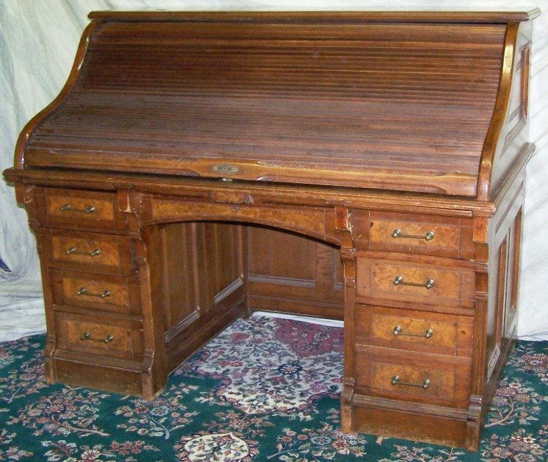***TURN OF THE CENTURY WALNUT ROLL TOP DESK: The C-roll opening to fitted interior with leather writing surface, fitted with 8 drawers surrounding knee hole, approximate height 48'', width 60'', depth 35 1/2''.
