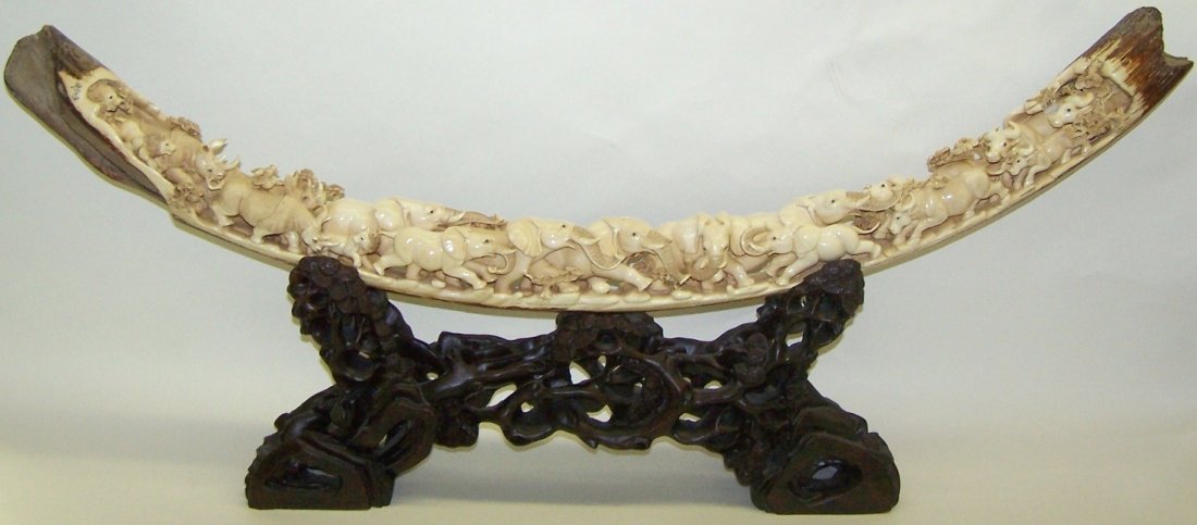 CHINESE CARVED MASTODON IVORY TUSK: Carved with water buffalo, rhinoceros, lion and elephant decoration, artist signed, approximate length 36'', raised on carved rosewood base. Note: Items containing ivory will only be shipped domestica