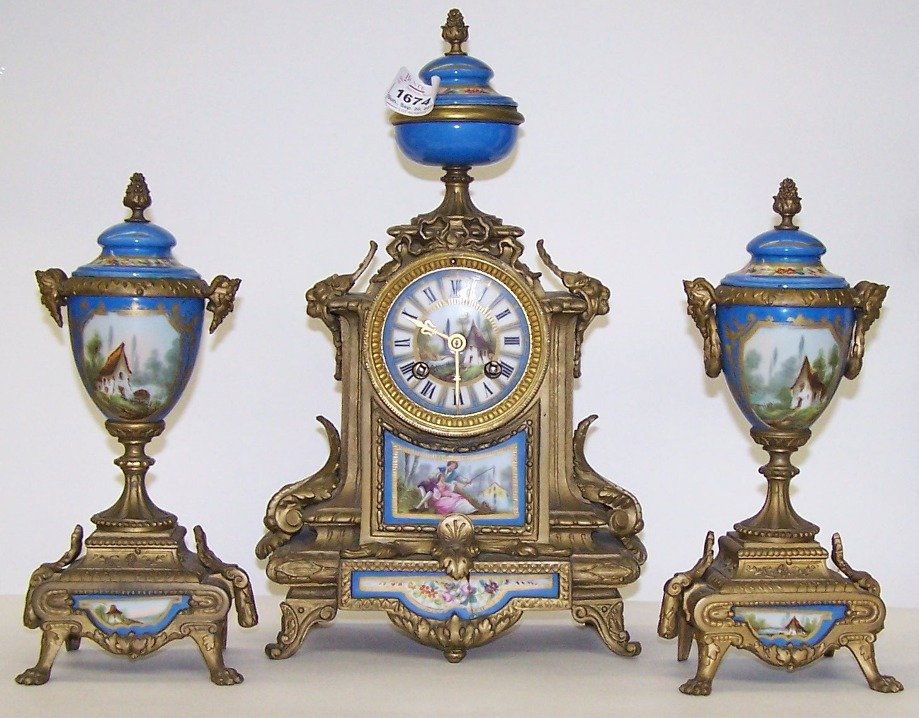 THREE PIECE CLOCK GARNITURE SET: French clock fitted with time and strike movement, the porcelain dial having Roman numeral markers surrounding cottage scene, enclosed in brass and porcelain case, surmounted with urn, and having pane