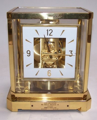 *LECOULTRE ATMOS MANTEL CLOCK: Having Roman Numerals and bar markers on a white and gilt finish dial, contained in a brass and glass case, approximate height 9", length 8 1/4", and depth 6 1/4".