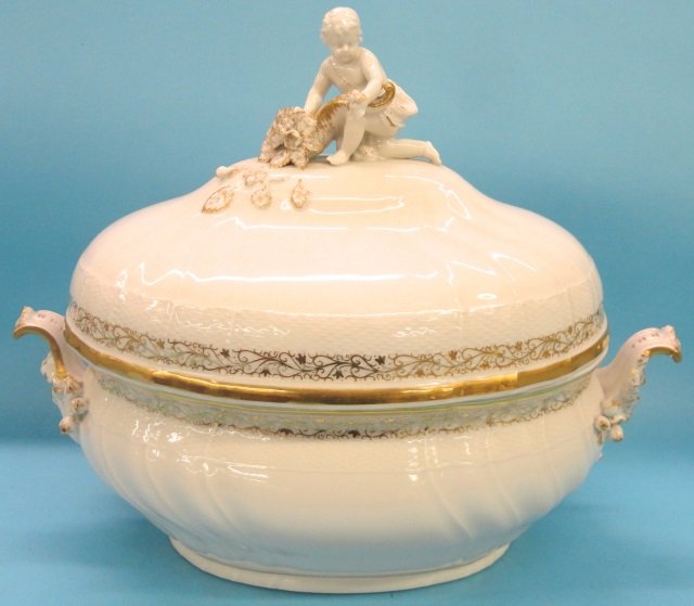 *KPM PORCELAIN 2-HANDLED TUREEN: Having floral decoration and gilt highlights, lid surmounted with applied figure of cherub with flowers, approximate height 12", length 15 1/2.