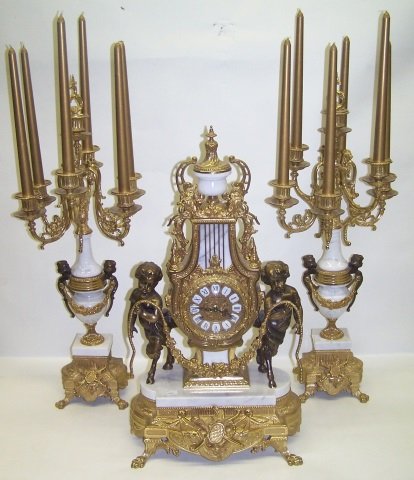 *3 PIECE CLOCK GARNITURE SET: Having French style clock fitted with time and strike movement, the brass dial having enamel Roman numeral markers enclosed in bronzed and marble case, decorated with urn, scroll work and pair of putt