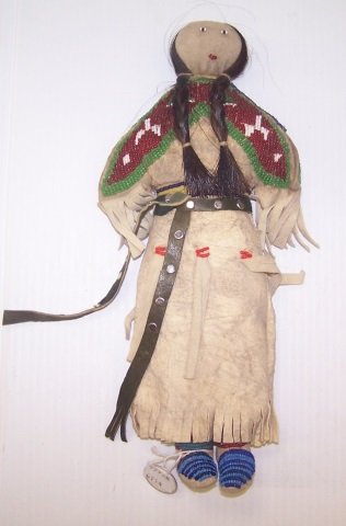 *SIOUX HIDE, CLOTH AND BEADED DOLL: Woman with red beaded yoke and concho, approximate length 11 1/4".