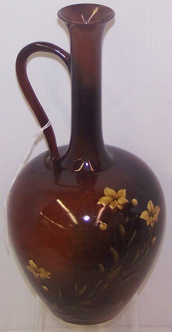 *ROOKWOOD ART POTTERY EWER: Decorated by Albert R. Valentien, with white lilies on a ground shaded brown and rust, marks include impressed Rookwood flame logo indicating date 1886, shape #262, R (for red clay), signed with artis