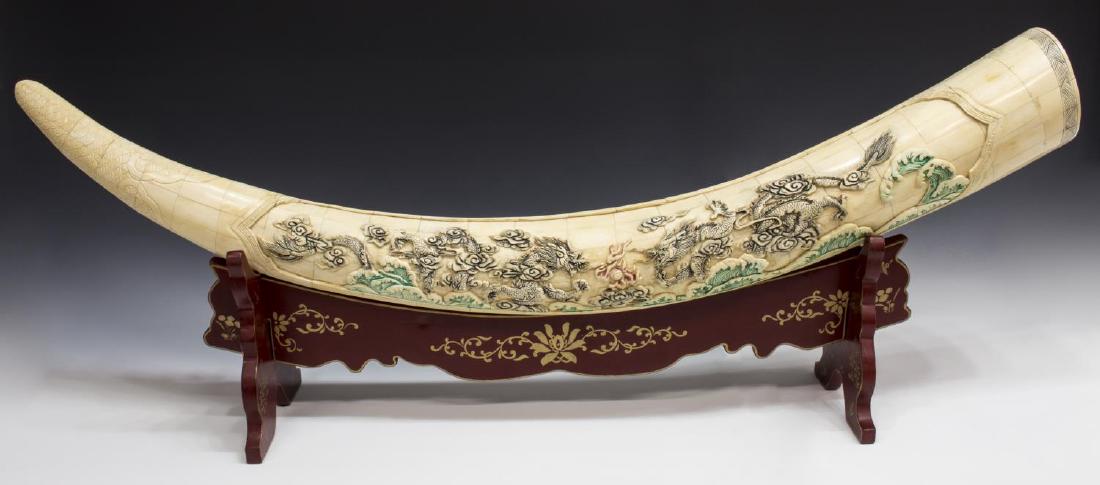 LARGE CHINESE CARVED & TILED BONE TUSK ON STAND: Large Chinese carved and tiled bone tusk, one side showing dragons in relief, the other etched with landscapes, carved clouds to tip, on painted wood stand, of three interlocking pieces, red with gilt
