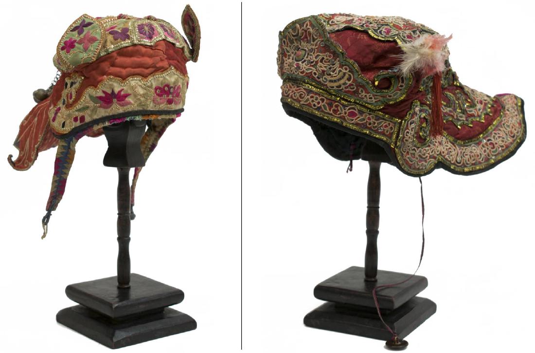 (2) ANTIQUE MONOGOLIAN EMBROIDERED CHILDREN'S HATS: (lot of 2) Antique Mongolian children's hats, both embroidered with flowers, heavy gilt thread: (1) floral decorated "ears", elongated back with bells verso, on a wood stand; (1) having thick and heav