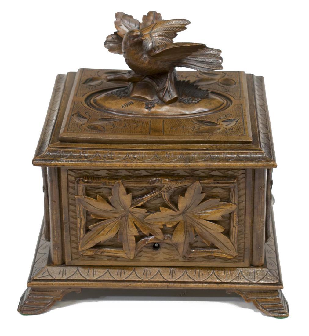 BLACK FOREST RELIEF CARVED BIRD & LEAVES TABLE BOX: Black Forest carved walnut table box, a perched bird on leafy branch, surmounting the box of square form, opening to later lined interior, relief carved leaves on three sides, the back incised, rising