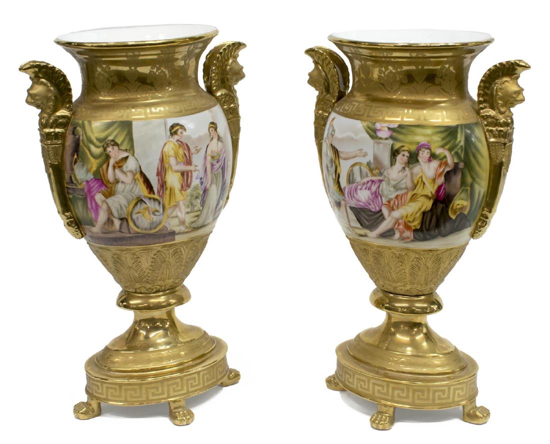 (2) GERMAN KPM STYLE GILT & HAND PAINTED URNS: (lot of 2) German K.P.M. style gilt and hand painted porcelain urns, each with an oval rim above winged griffin handles, accented by key fret bands, and figural reserves depicting Greco Roman figural