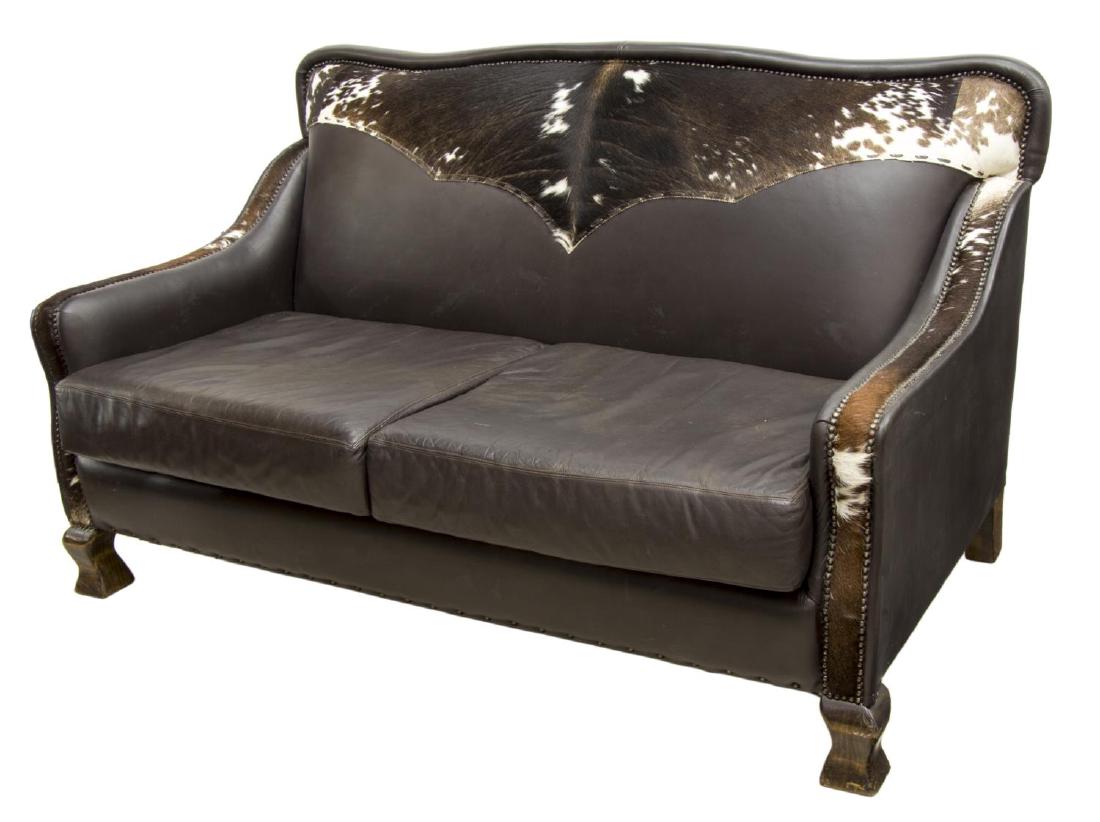 CONTEMPORARY LEATHER & COWHIDE TWO-SEAT SOFA: Contemporary brown leather two-seat sofa, cupid's bow shaped back, having cow hide and nail head accents, with two removable cushions, rising on square baluster shaped feet, approx 39.5"h, 67.5"w, 36.