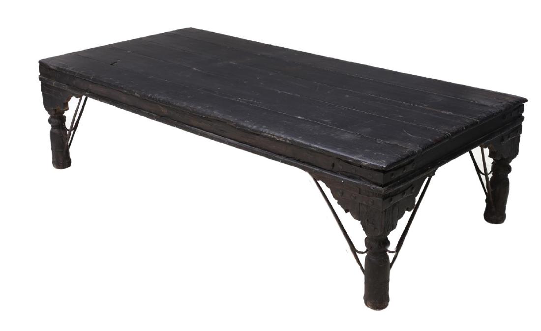 BRITISH COLONIAL CARVED TEAKWOOD COFFEE TABLE: British Colonial carved ebonized teakwood coffee table, the thick rectangular top rising on turned legs with wrought iron supports, 22"h, 81"w, 41"d Start Price: $100.00