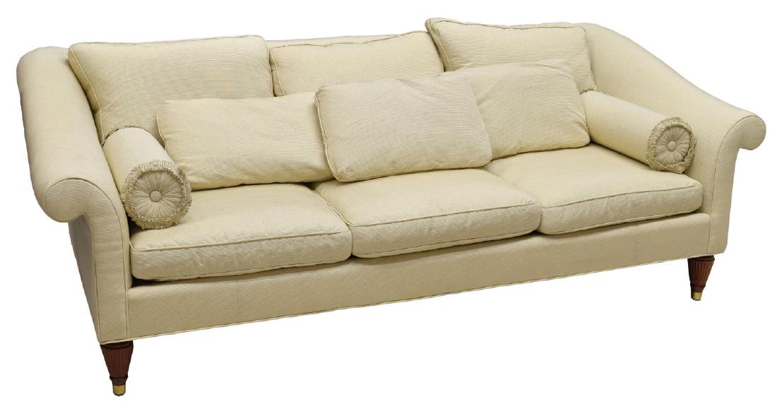 BAKER FURNITURE COMPANY THREE SEAT SOFA: Sofa by Baker Furniture Company, upholstered in beige corded fabric with three seat and back cushions, two throw pillows, two bolsters, rising on tapered ribbed supports with brass capped feet, some l