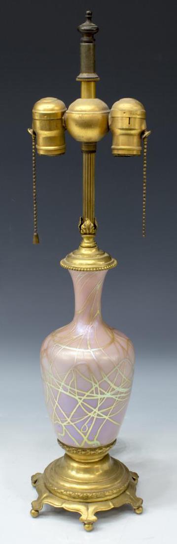 OPALESCENT PINK ART GLASS TABLE LAMP: Art glass table lamp, having gilt bronze hardware, acorn finial to top, over fluted standard, issuing two light fixtures, vasiform pink opalescent art glass body with cream colored streaks, rising on 