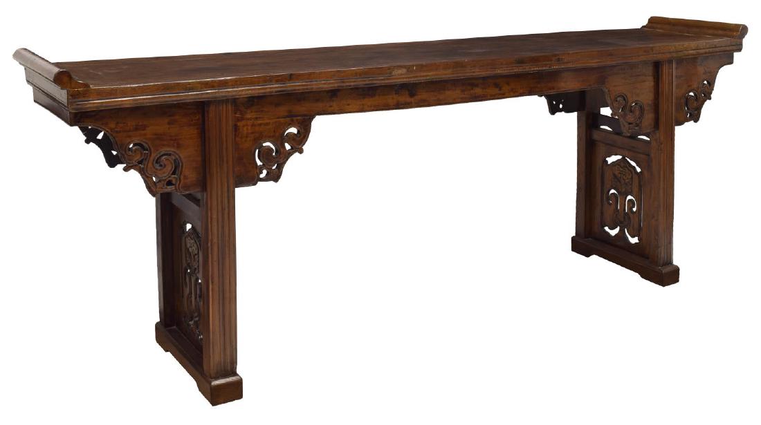 CHINESE CARVED ELMWOOD ALTAR TABLE: Chinese carved elmwood altar table, rectangular top with shaped ends, over pierced and carved accented apron, rising on pierced and carved trestle legs, approx 36"h, 96.5"w, 17.75"d Start Price: $250.