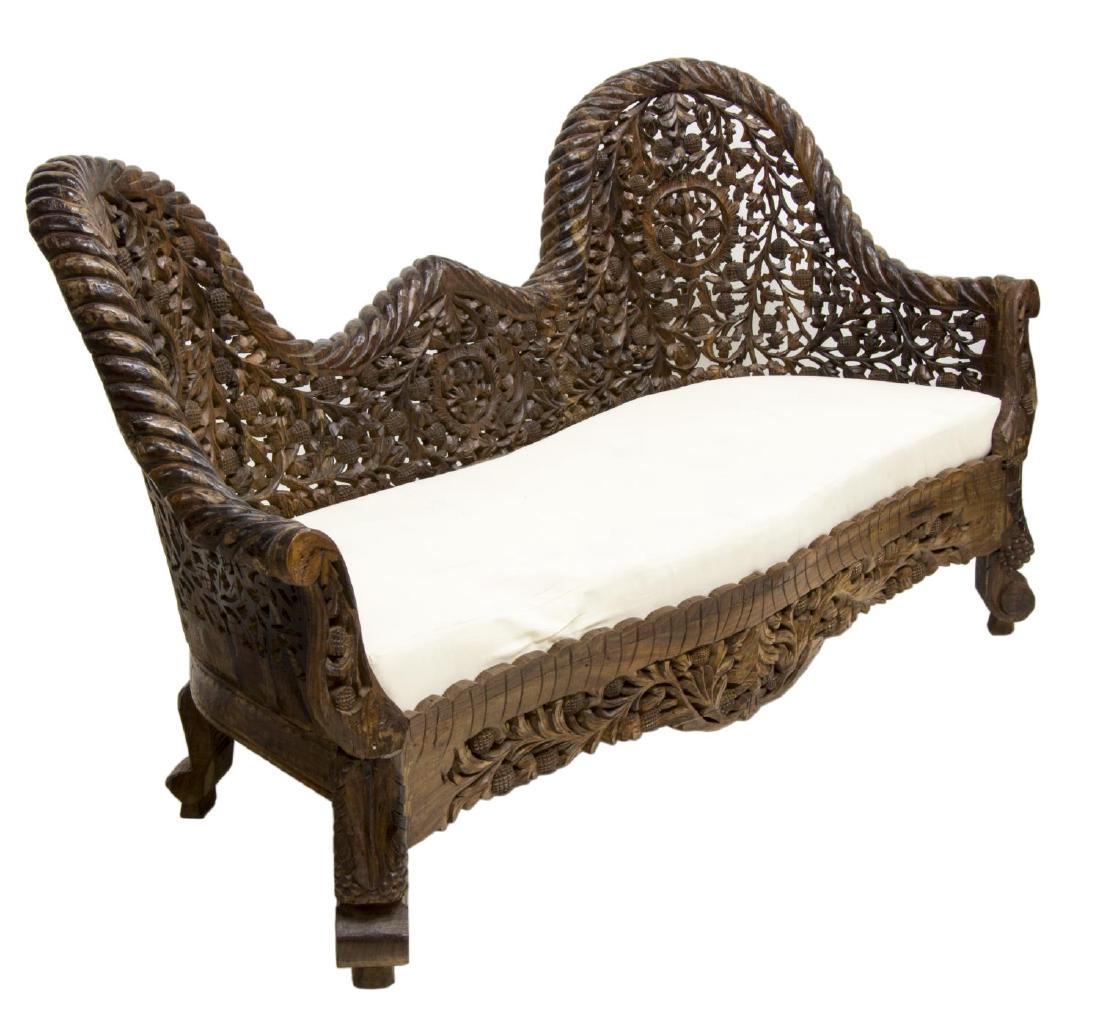 ANGLO-INDIAN HIGHLY CARVED TEAKWOOD SOFA: Anglo-Indian teakwood sofa, profusely pierce carved with flowering vines and foliates, the undulating back over upholstered seat, rising on grape cluster carved front supports, approx. 36.5"h, 66.5"w,