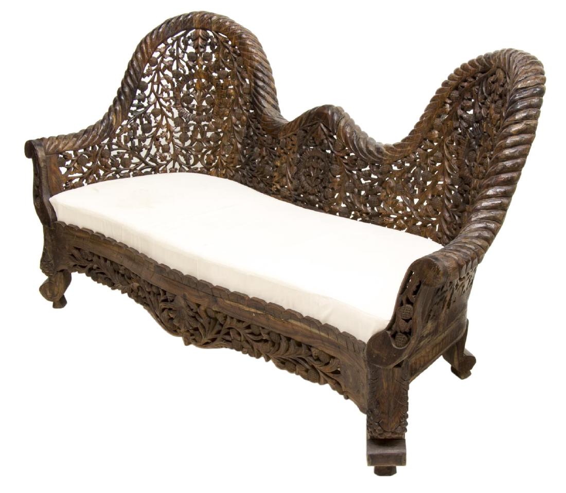 ANGLO-INDIAN HIGHLY CARVED TEAKWOOD SOFA: Anglo-Indian teakwood sofa, profusely pierce carved with flowering vines and foliates, the undulating back over upholstered seat, rising on grape cluster carved front supports, 36.5"h, 66.5"w, 25"d St