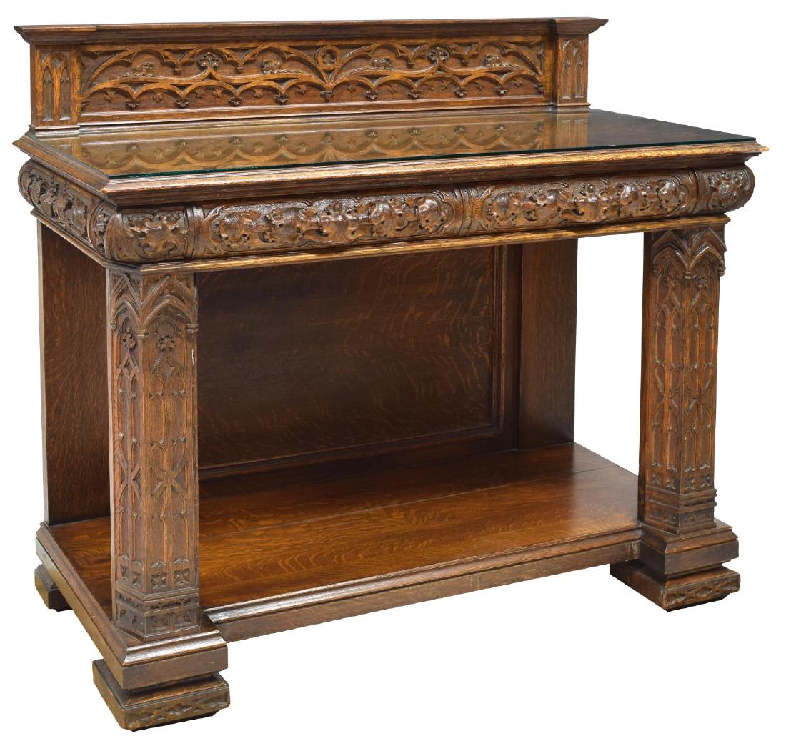 GOTHIC REVIVAL CARVED TRACERY FIGURED OAK SERVER: Gothic Revival figured oak server, early 20th c., raised back with carved tracery, over tabletop surface with glass top, over two drawers with foliate carved fronts, rising on legs with carved window 