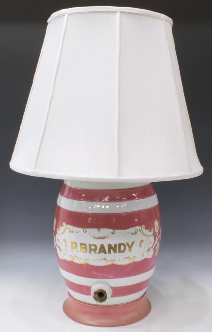 ENGLISH PORCLEAIN BRANDY BARREL TABLE LAMP: English porcelain "P. Brandy" barrel, now mounted as a table lamp, pink and white porcelain on a pink foot, later shade, lacking spigot, intact with crazing, old hairlines to top, approx 29.5"h (to ha