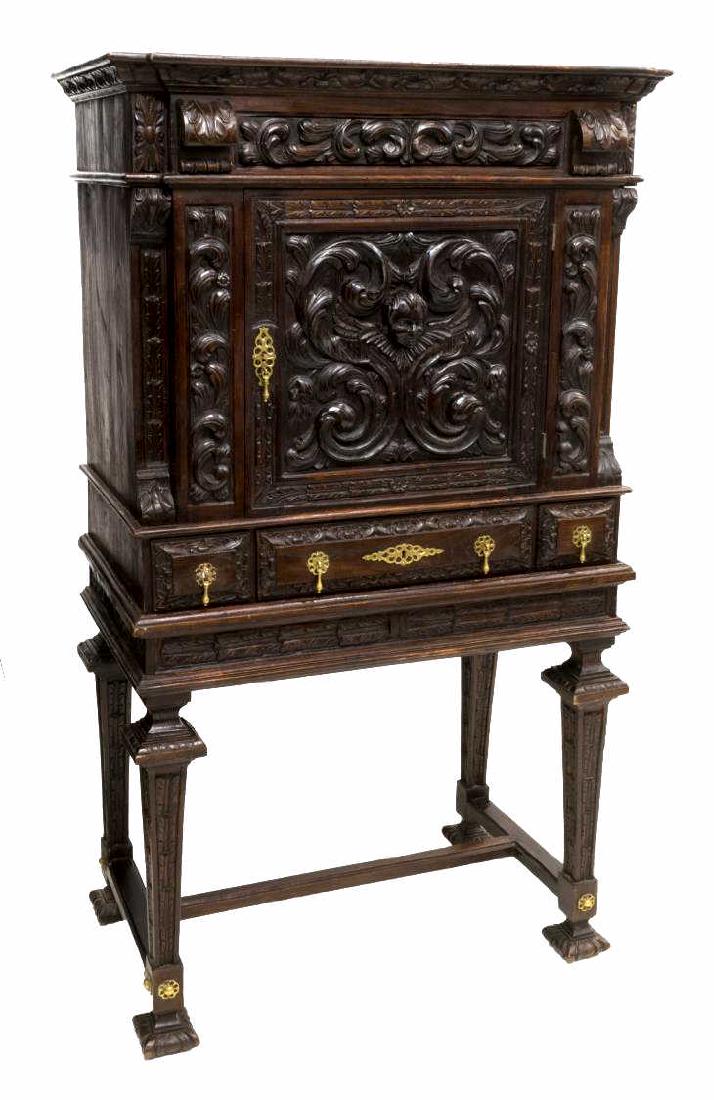 SPANISH RENAISSANCE REVIVAL HEAVILY CARVED CABINET: Spanish Renaissance revival heavily carved oak cabinet, 19th c., with scroll and acanthus designs, the cabinet door with a winged cherub mask to center, interior fitted with shelves, above three short