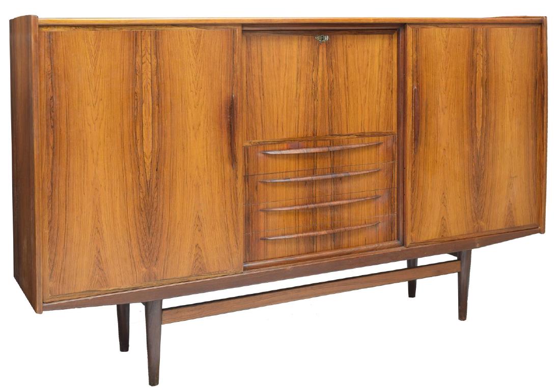 DANISH MID-CENTURY MODERN ROSEWOOD SIDEBOARD: Danish mid-century modern rosewood sideboard, c. 1960s, having a fall front center opening to shelved interior, above four drawers, sliding side doors open to reveal shelving and tray drawer, on cylin