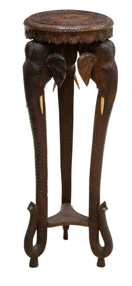 ELABORATE FIGURAL CARVED PEDESTAL, INDIA: Elaborately carved pedestal, India, having top with vines, flowers and center rosette, with shelf below, resting on legs in shape of elephant faces and trunks, with inset tusks, approx 35"h, 13.25"dia