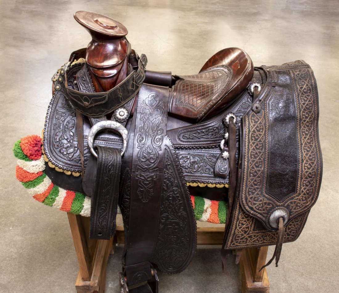 ORNATE SILVER ACCENTED CHARRO HORSE SADDLE: (lot) Ornately tooled leather Charro horse saddle bearing the label of Ignacio Hernandez, Colima, Mexico, accented with engraved silver overlaid on nickel conchos, rigging dees and stirrups, 14" seat,